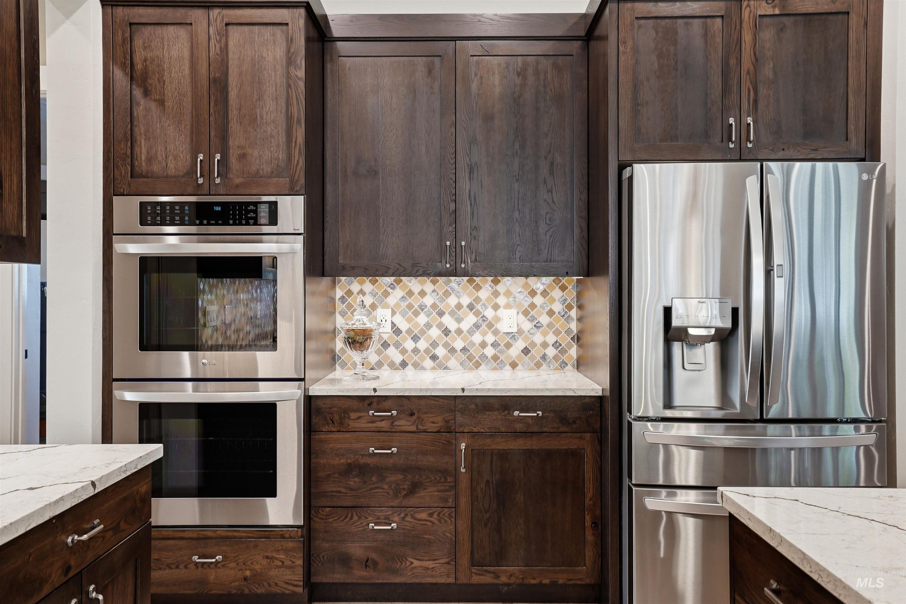 24165 Boer Goat Avenue Caldwell, ID 83607 - Photo 12 of 34 Kitchen featuring rich wood cabinetry, stainless steel double ovens, a stainless steel French door refrigerator, white countertops, and a mosaic tile backsplash