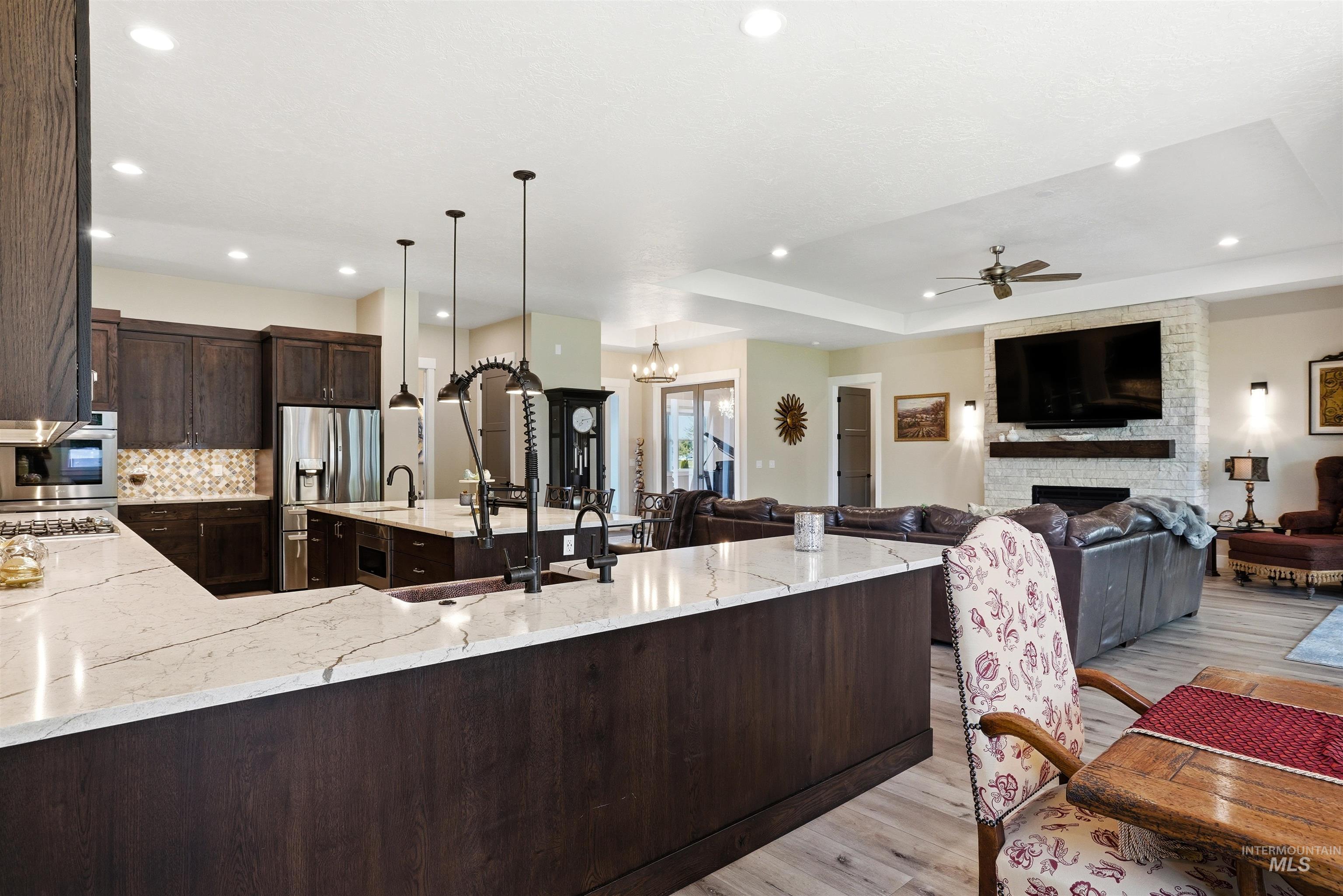 24165 Boer Goat Avenue Caldwell, ID 83607 - Photo 15 of 34 Open-concept living space featuring a kitchen with dark wood-finish cabinetry, light stone countertops, and stainless steel appliances