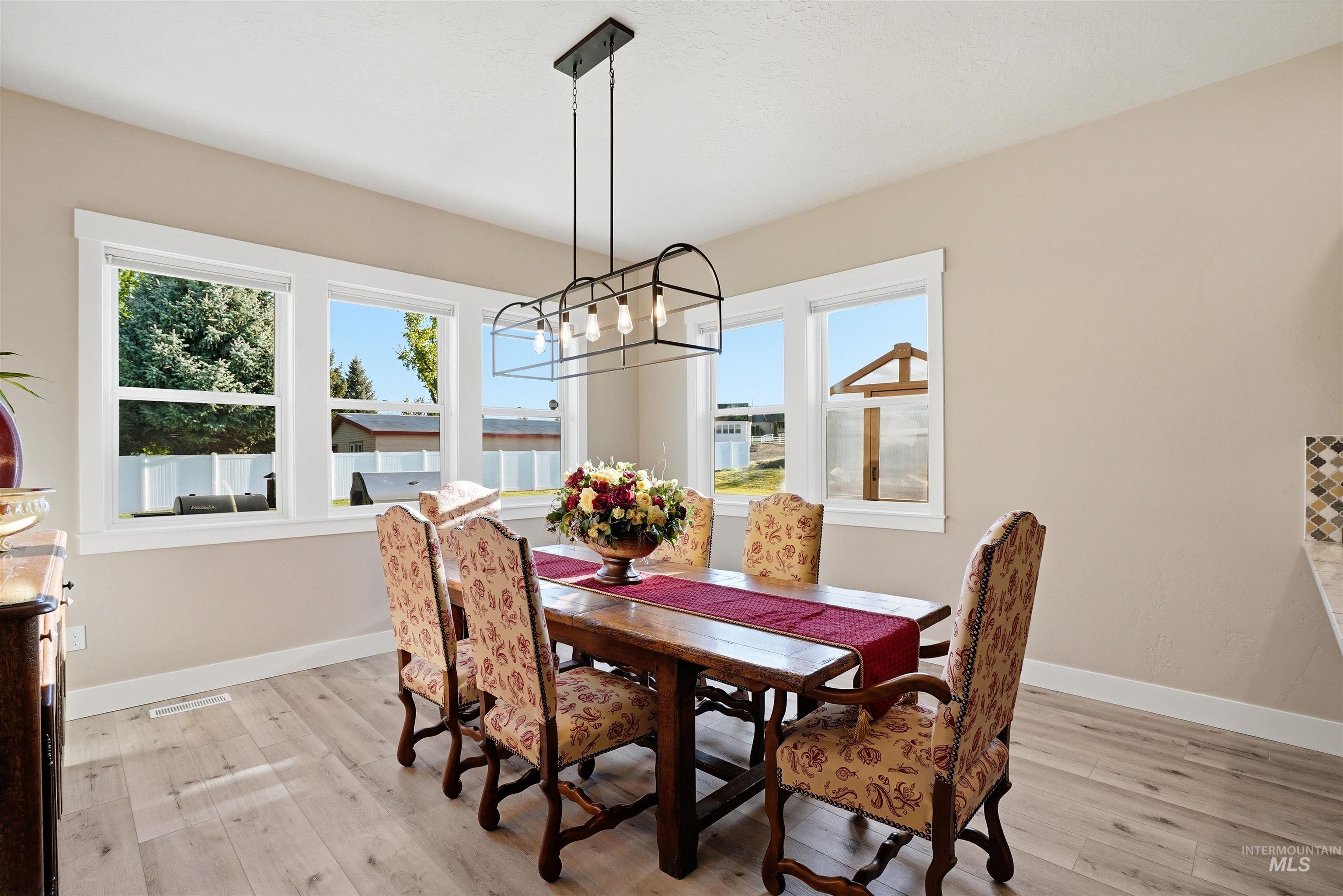 24165 Boer Goat Avenue Caldwell, ID 83607 - Photo 16 of 34 Dining area featuring wood-finish flooring, a contemporary linear chandelier, multiple windows with white trim, and light neutral wall tones
