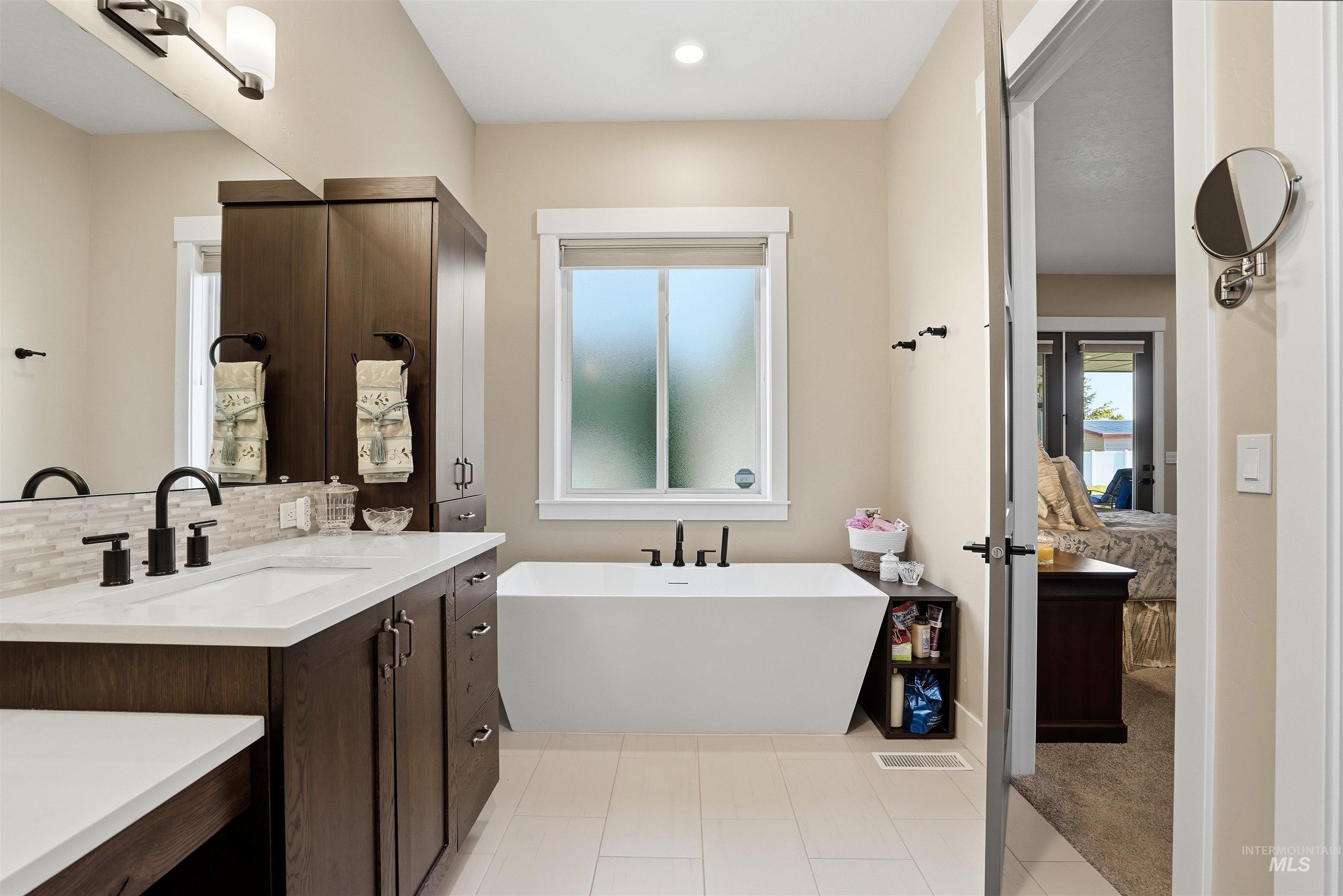 24165 Boer Goat Avenue Caldwell, ID 83607 - Photo 20 of 34 Contemporary bathroom featuring a freestanding tub, dual-sink vanity with dark wood cabinetry, white countertops, and matte black fixtures