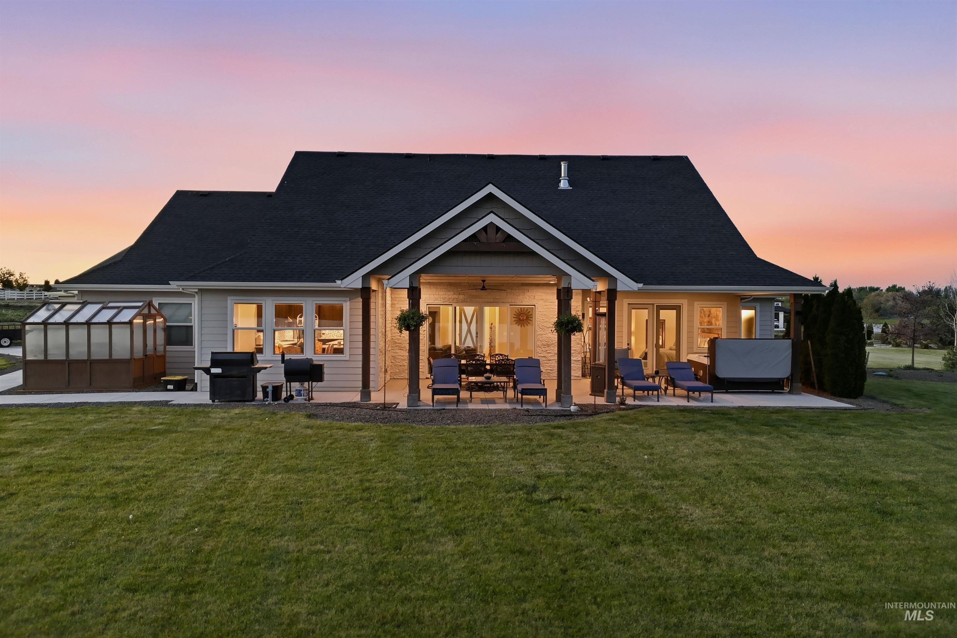 24165 Boer Goat Avenue Caldwell, ID 83607 - Photo 30 of 34 Rear exterior featuring a covered patio with stone-wrapped columns, an expansive concrete patio, and a dedicated greenhouse structure
