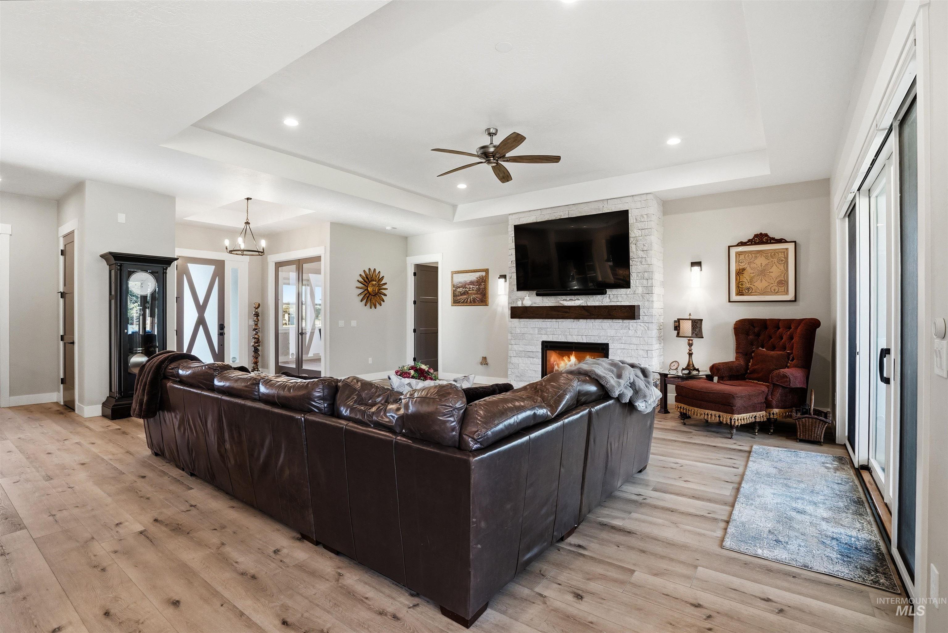 24165 Boer Goat Avenue Caldwell, ID 83607 - Photo 8 of 34 Spacious living area featuring light wood-finish flooring, a white brick fireplace with a wood mantle, and a tray ceiling with recessed lighting
