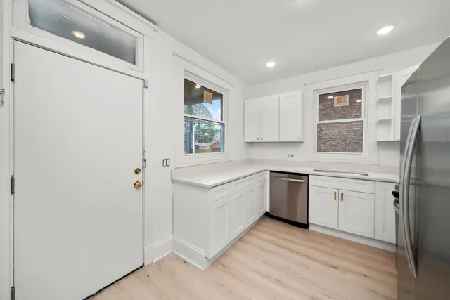 a large kitchen with a refrigerator a sink dishwasher a stove and white cabinets with wooden floor