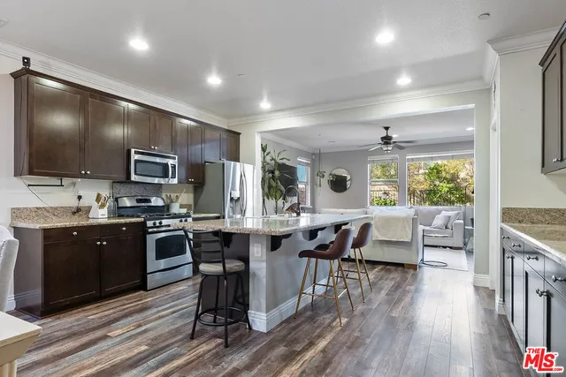 a open kitchen with stainless steel appliances granite countertop a stove top oven a sink dishwasher a dining table and chairs with wooden floor