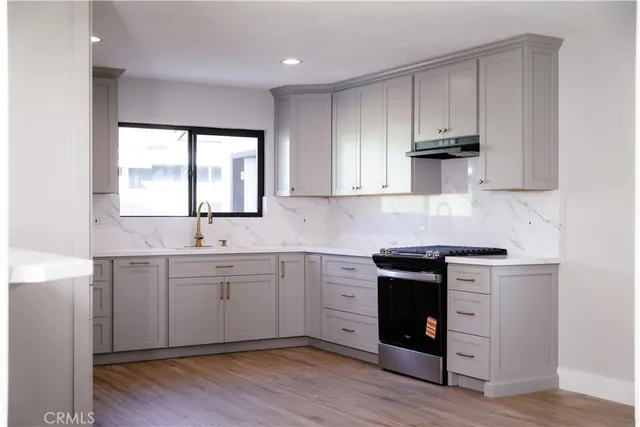 a kitchen with stainless steel appliances granite countertop white cabinets a stove a sink and dishwasher with wooden floor