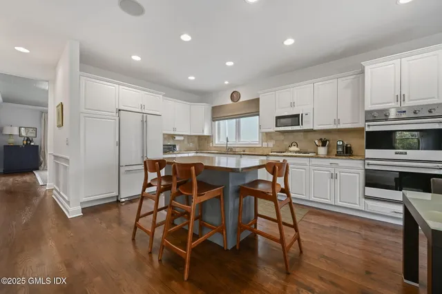 a kitchen with stainless steel appliances a microwave a stove a sink a refrigerator and white cabinets with wooden floor