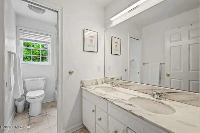 a bathroom with a granite countertop sink toilet a large mirror a vanity and a window