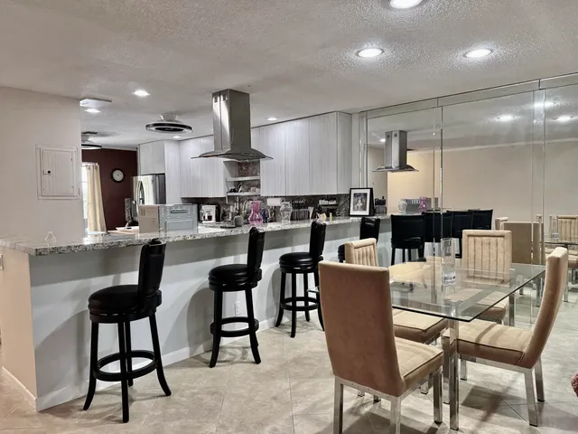 a dining area with stainless steel appliances kitchen island granite countertop a dining table chairs and a refrigerator