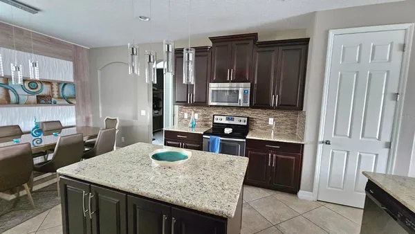 a kitchen with stainless steel appliances granite countertop a refrigerator a sink dishwasher a stove and a dining table with wooden floor