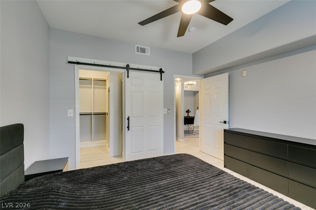 7255 West Sunset Road, Unit 1103 Las Vegas, NV 89113 - Photo 34 of 35 A well-lit bedroom features a ceiling fan, a walk-in closet with sliding barn doors, and light wood flooring.