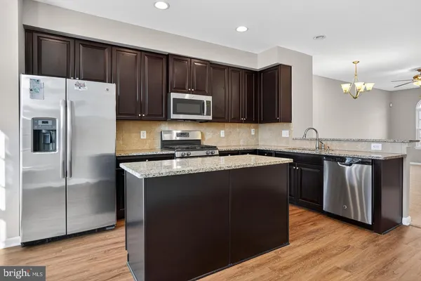 a kitchen with granite countertop a refrigerator a sink a stove a microwave and wooden floor