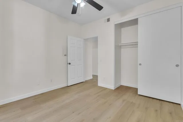 an empty room with wooden floor chandelier fan and refrigerator
