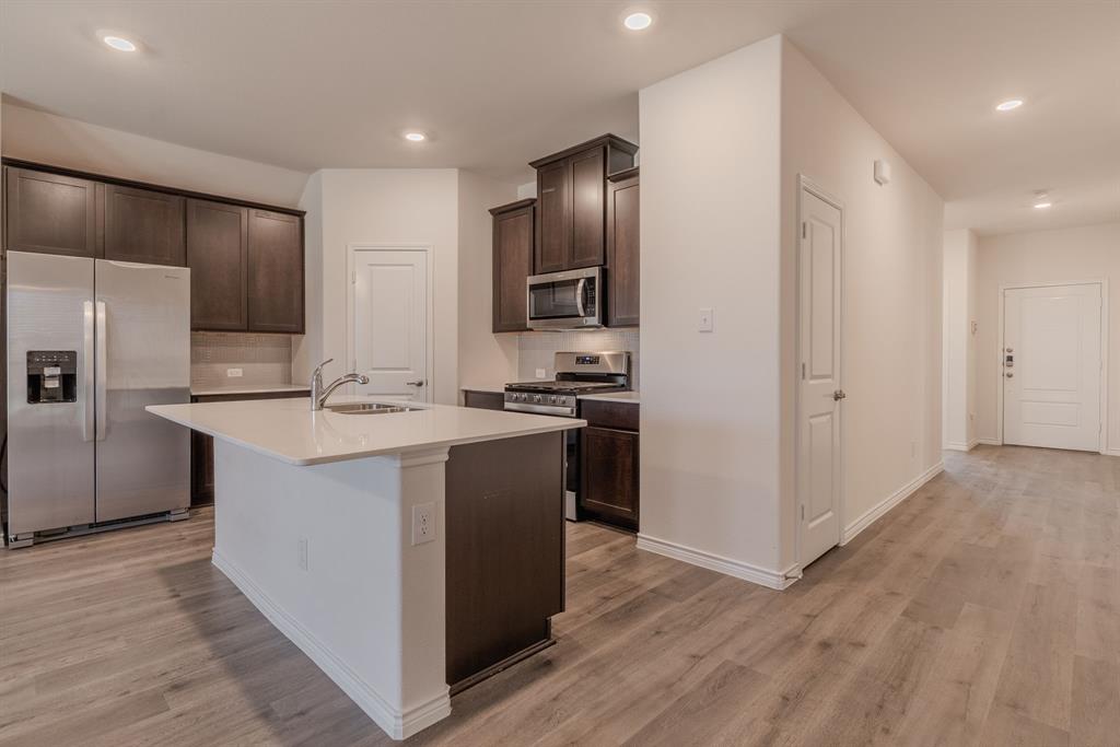 2902 Trusting Way Aubrey, TX 76227 - Photo 6 of 38 Kitchen featuring dark wood-finish cabinetry, stainless steel appliances, a center island with a sink, and light-toned countertops