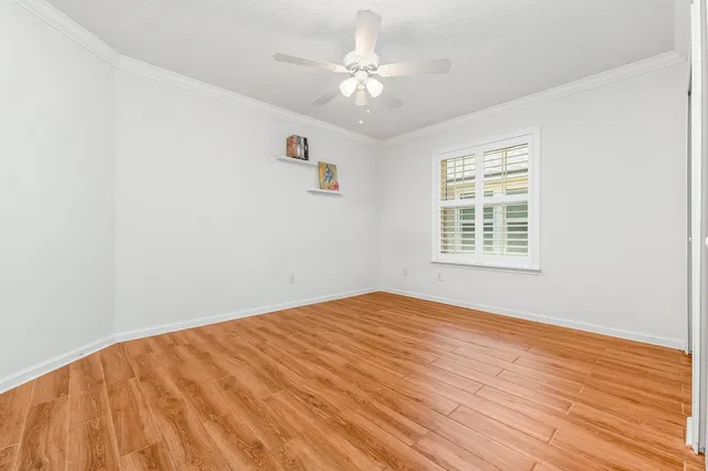 an empty room with wooden floor chandelier fan and windows