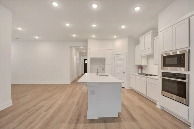 a large kitchen with stainless steel appliances kitchen island granite countertop a stove a sink a refrigerator and white cabinets with wooden floor