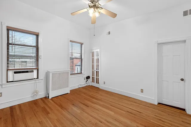 an empty room with wooden floor chandelier fan and windows