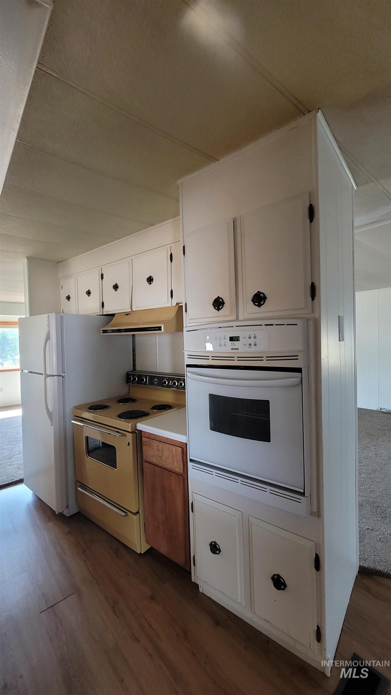 2122 Highway 95 Council, ID 83612 - Photo 13 of 31 Kitchen with white appliances, dark wood-style flooring, white cabinets, light countertops, and under cabinet range hood