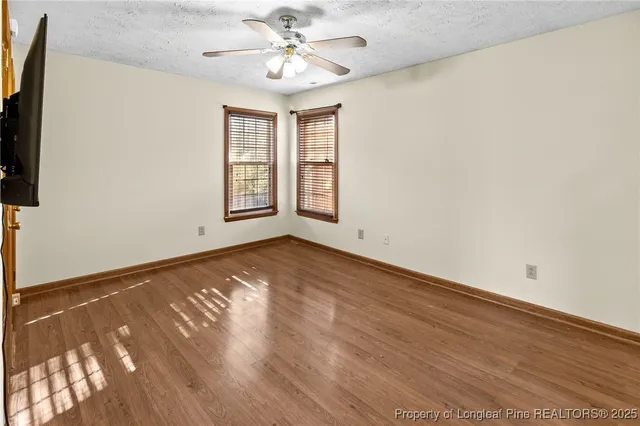 a view of an empty room with wooden floor and a ceiling fan