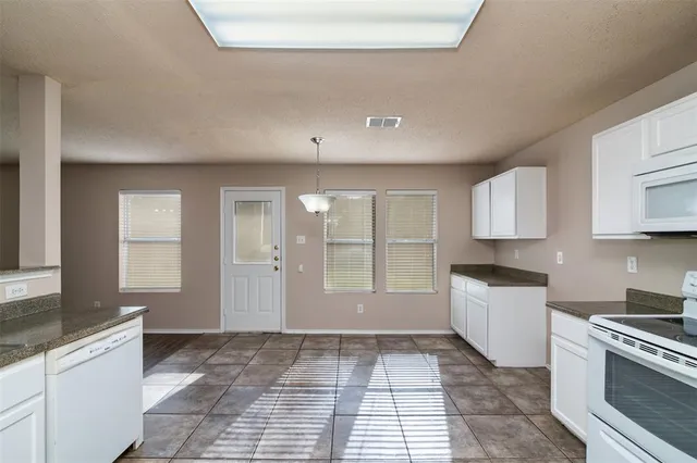 a large white kitchen with granite countertop a stove a sink a window and white cabinets