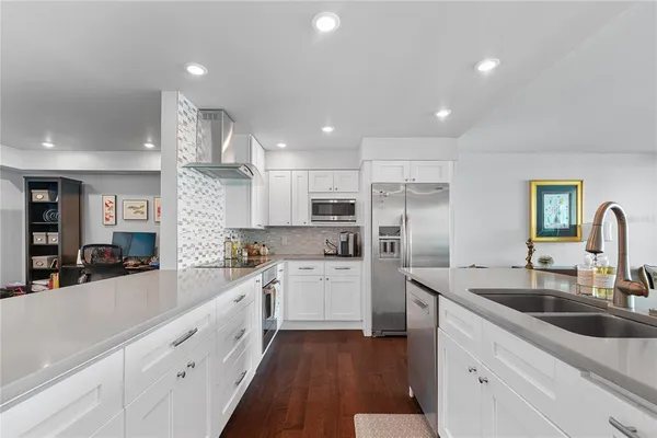 a open kitchen with stainless steel appliances granite countertop a sink dishwasher a refrigerator and white cabinets with wooden floor