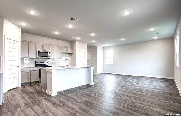 a kitchen with stainless steel appliances granite countertop a stove top oven a sink dishwasher a refrigerator and white cabinets with wooden floor