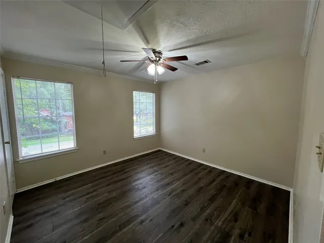 an empty room with wooden floor fan and windows