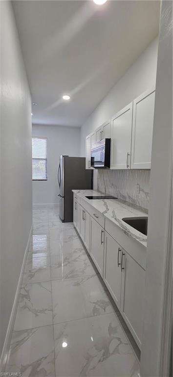 598 2nd Street Southeast Naples, FL 34117 - Photo 30 of 40 Kitchen featuring white cabinets, light stone countertops, light marble finish floors, freestanding refrigerator, and backsplash