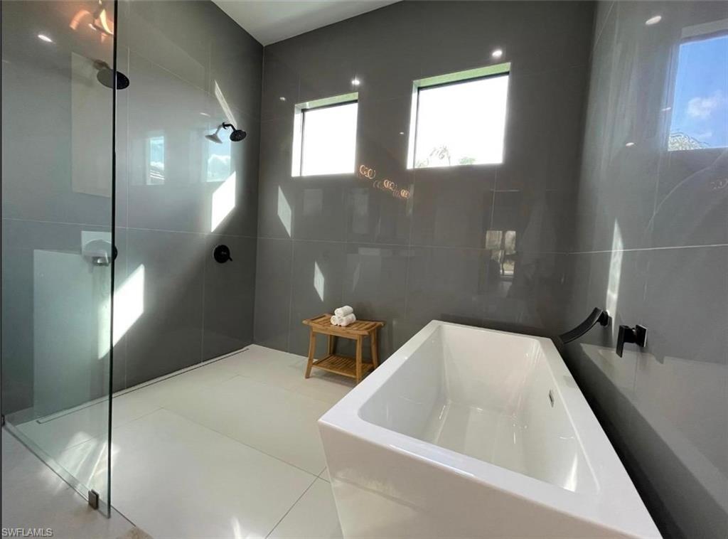 687 23rd Street Southwest Naples, FL 34117 - Photo 16 of 40 Full bathroom featuring a freestanding tub, walk in shower, tile walls, and tile patterned flooring