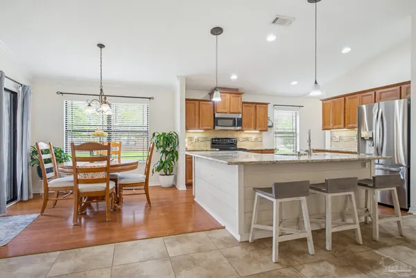 a kitchen with stainless steel appliances kitchen island granite countertop a stove a refrigerator and a dining table with wooden floor