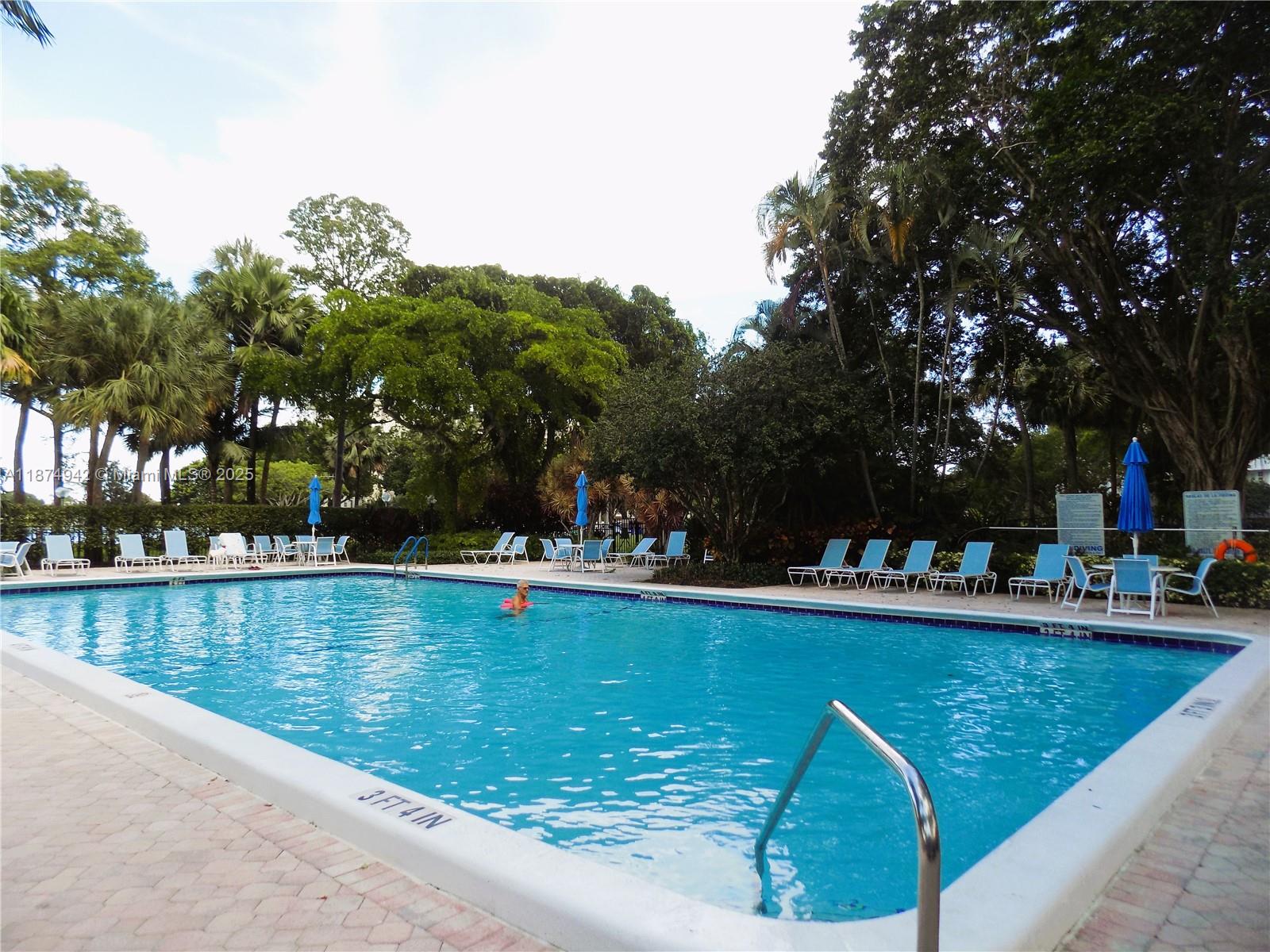 3100 North Course Lane, Unit 502 Pompano Beach, FL 33069 - Photo 30 of 32 a view of a swimming pool that has lawn chairs and a dining table under an umbrella