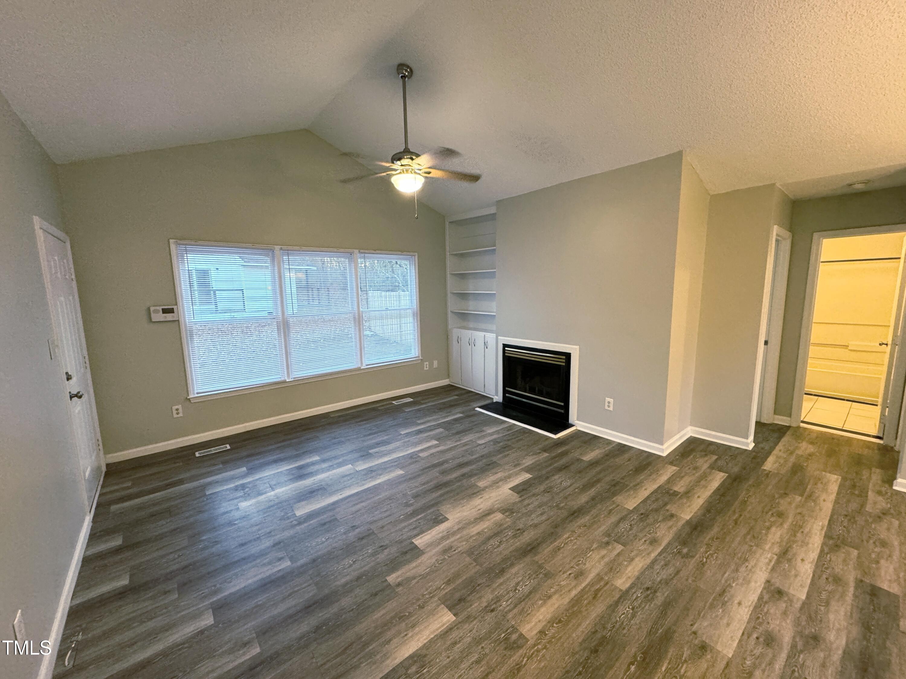 456 Dickens Drive Raleigh, NC 27610 - Photo 10 of 33 an empty room with wooden floor fireplace and windows
