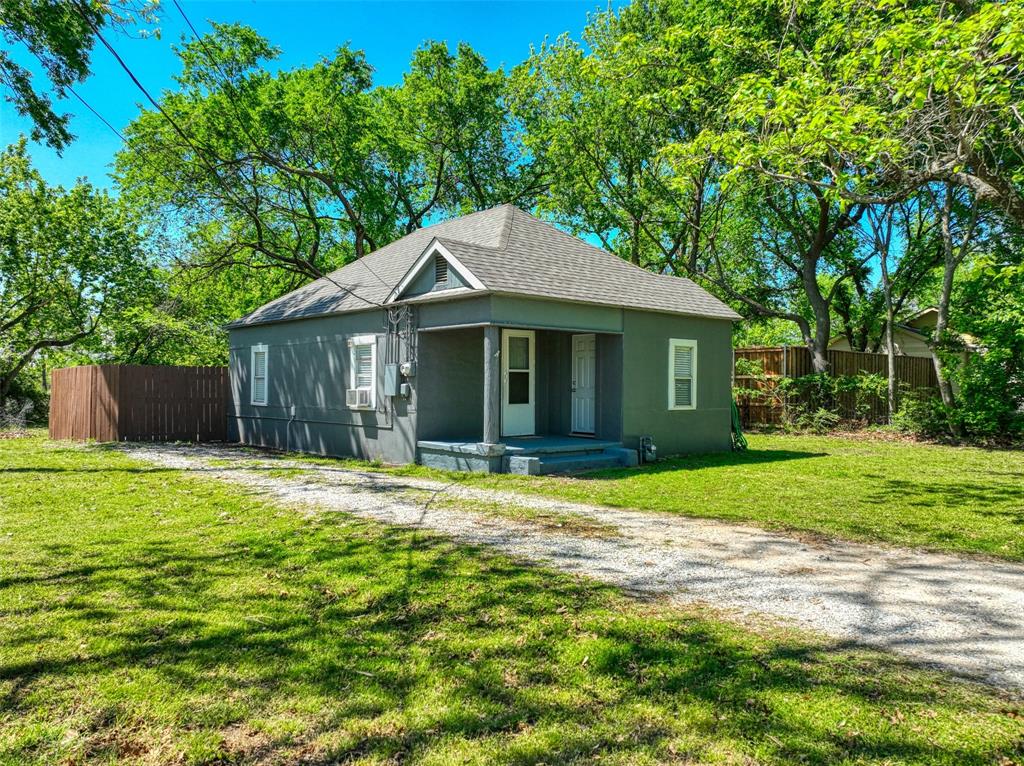 The property features a gray exterior with white trim, a covered porch, and a gravel driveway