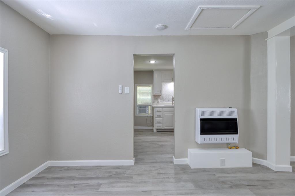 311 West McKinney Street Pilot Point, TX 76258 - Photo 18 of 33 Living area featuring light gray walls, light wood-style flooring, a wall-mounted heater, and a doorway leading to a kitchen with white cabinetry
