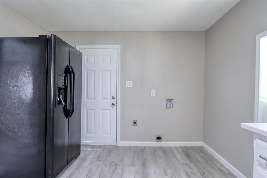 311 West McKinney Street Pilot Point, TX 76258 - Photo 25 of 33 The property features a black side-by-side refrigerator, light-colored walls, and wood-look flooring