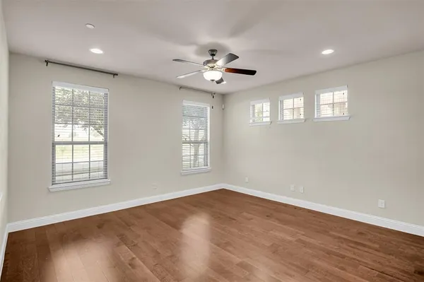 an empty room with wooden floor ceiling fan and windows