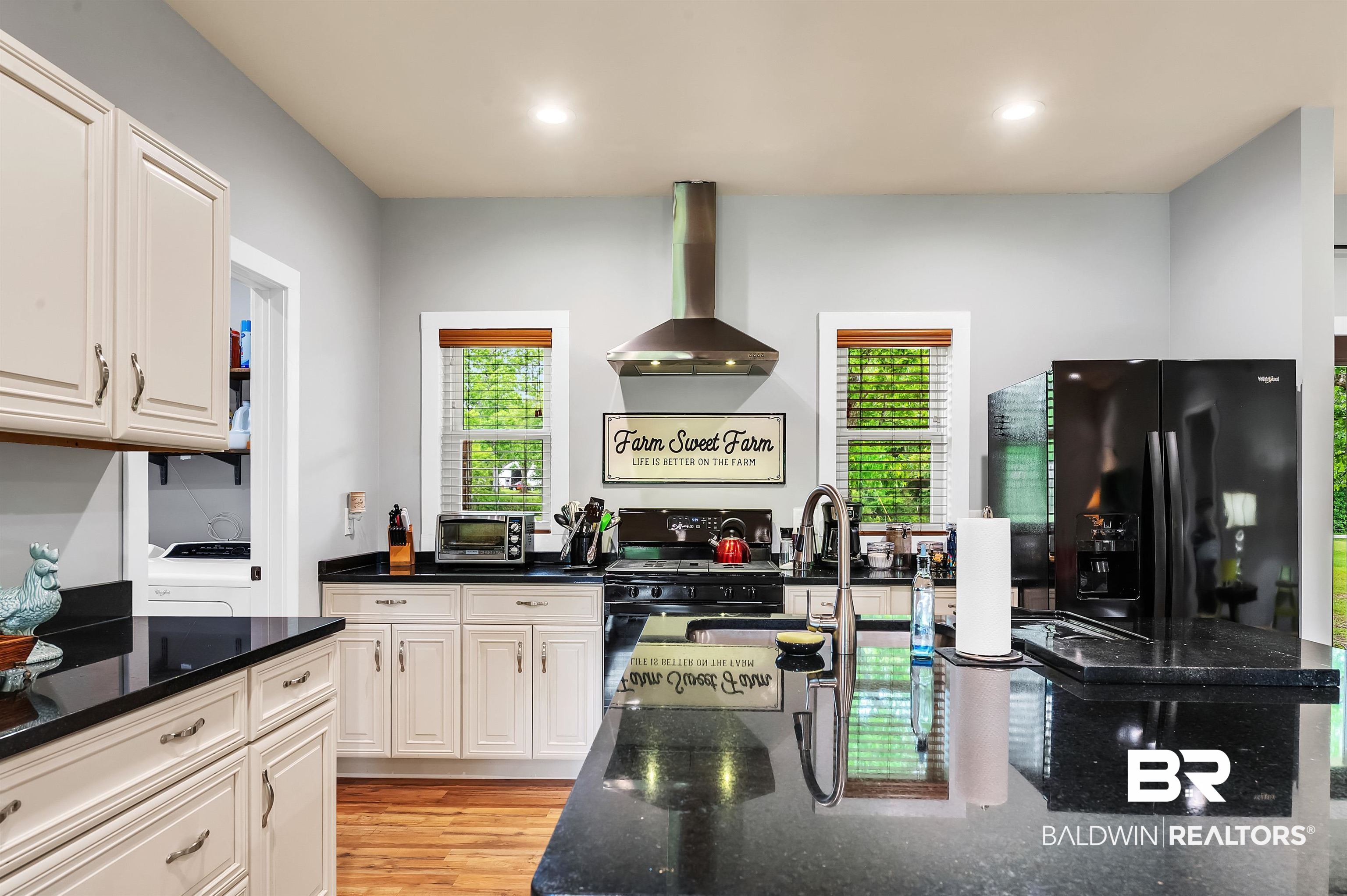 13827 County Road 83 Elberta, AL 36530 - Photo 21 of 38 Kitchen with wall chimney range hood, black appliances, white cabinetry, dark stone counters, and a sink