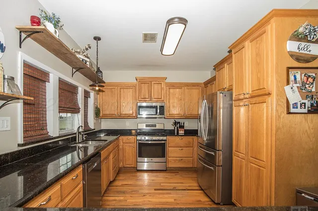 a kitchen with granite countertop a refrigerator a sink and dishwasher a stove top oven with wooden floor