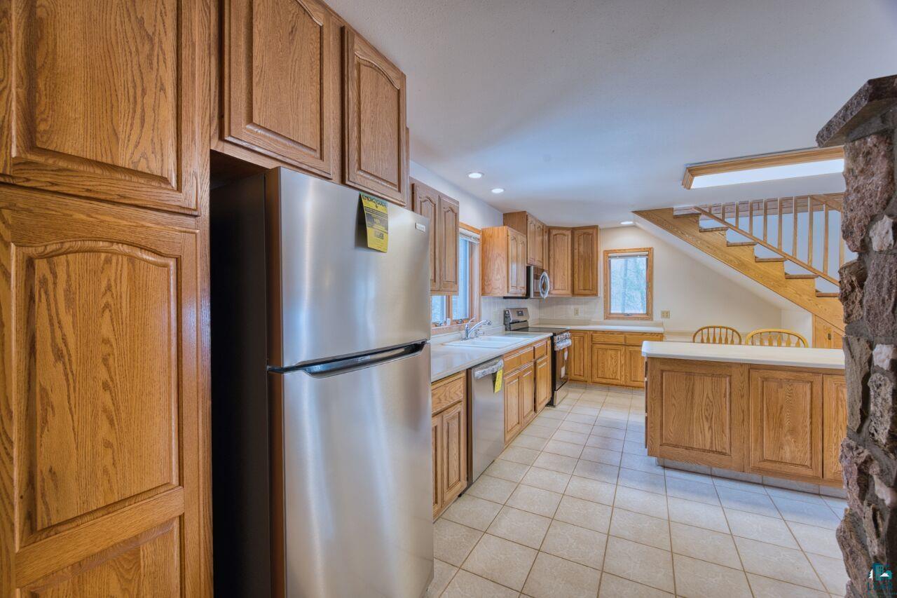 6312 Juniper Lane Gilbert, MN 55741 - Photo 11 of 50 Kitchen with appliances with stainless steel finishes, light tile patterned flooring, a sink, light countertops, and brown cabinets