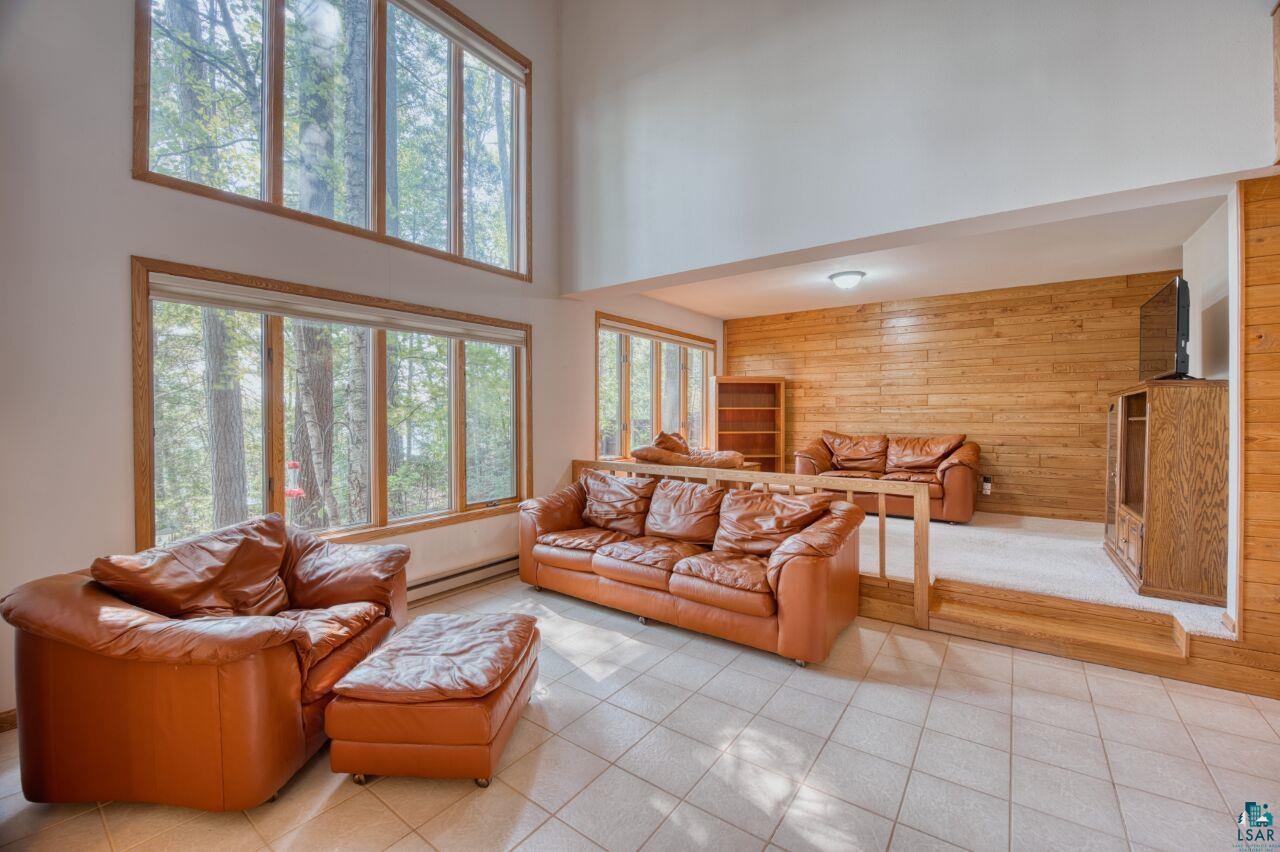 6312 Juniper Lane Gilbert, MN 55741 - Photo 2 of 50 Tiled living room featuring a towering ceiling, a baseboard radiator, wooden walls, and a healthy amount of sunlight