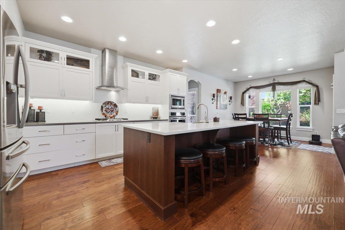 1303 West Brando Street Meridian, ID 83646 - Photo 10 of 49 Expansive kitchen featuring a large central island with seating, stainless steel appliances, white cabinetry with upper glass-front accents, and wood-finish flooring