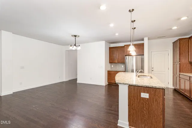 a kitchen with stainless steel appliances kitchen island granite countertop wooden floor sink and a refrigerator