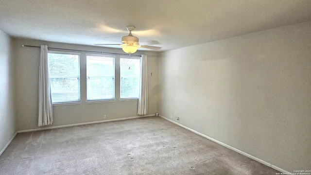 an empty room with windows and chandelier fan