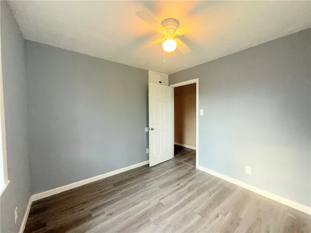 a view of an empty room with wooden floor and fan