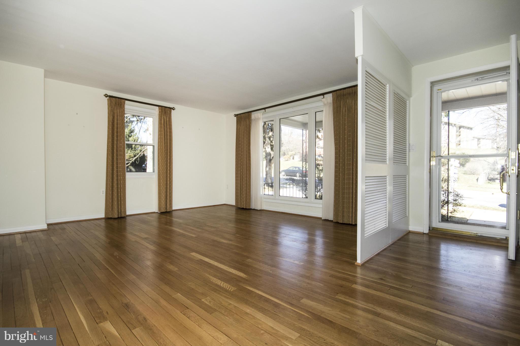 1305 Knightswood Road Baltimore, MD 21239 - Photo 3 of 29 an empty room with wooden floor and windows with curtains