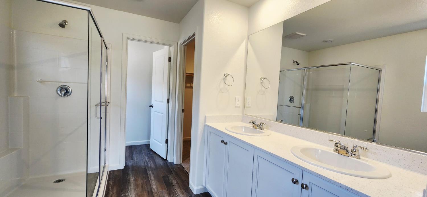 224 Teton Rnch Way Patterson, CA 95363 - Photo 8 of 13 Primary bathroom featuring double vanity, a stall shower, dark wood-style flooring, and a walk in closet
