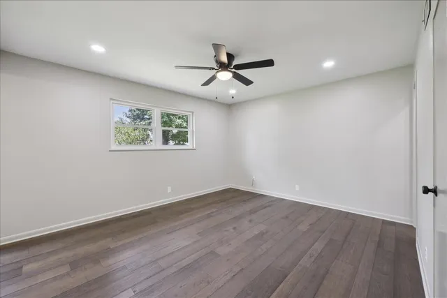 an empty room with wooden floor ceiling fan and windows