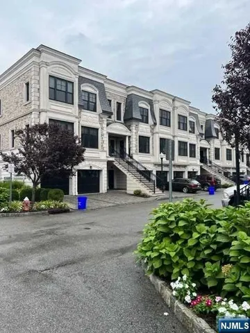 a front view of a building with garden and parking