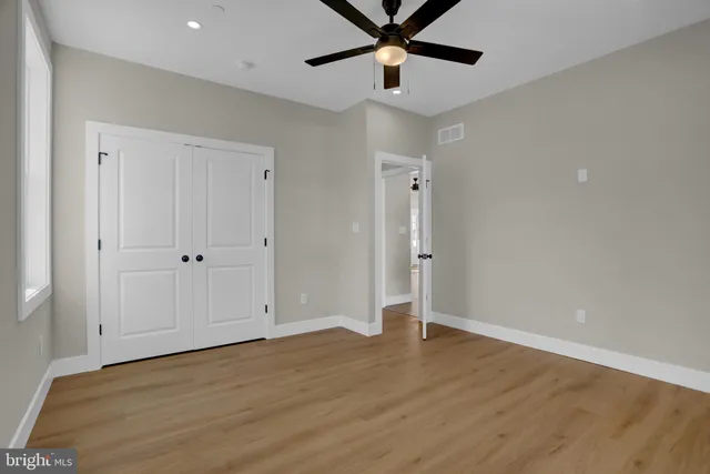 an empty room with wooden floor a ceiling fan and windows