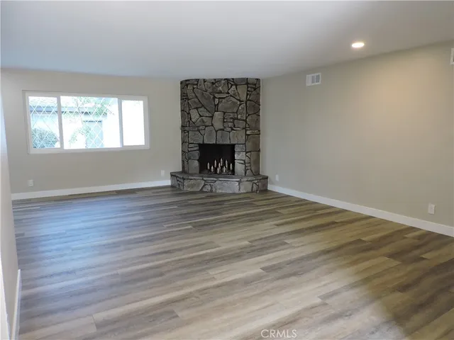 a view of an empty room with wooden floor fireplace and a window