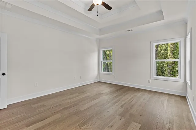 an empty room with wooden floor chandelier fan and windows